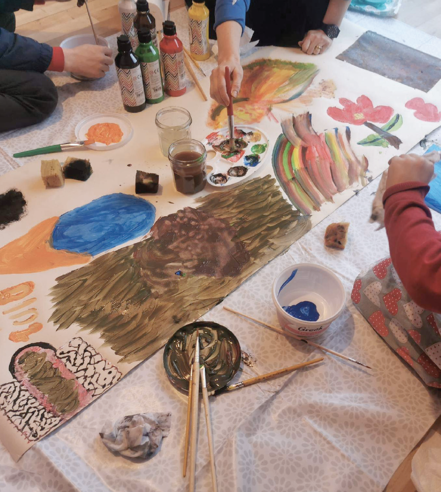 A photograph of a therapeutic arts workshop with children using poster paints expressively on a large scale format