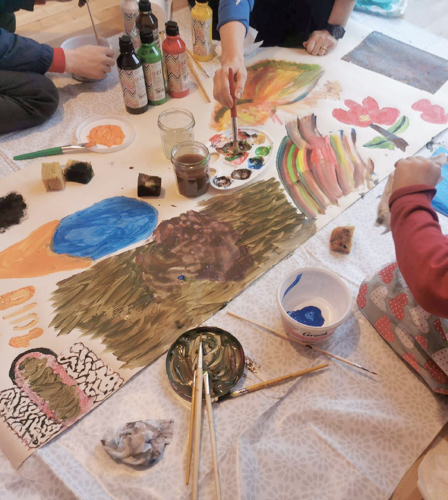 A photograph of a therapeutic arts workshop with children using poster paints expressively on a large scale format