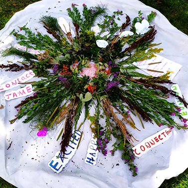 A large mandala pattern created from flowers and plants in a park, decorated with hand-written positive words.